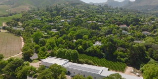 在绿树环绕的住宅区或村镇上空飞行。向上倾斜，在背景中显示山脉。南非开普敦