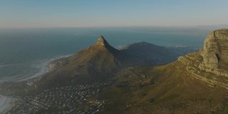 向前飞越桌山国家公园。城市周围是丘陵和岩石山峰。海洋在后台。南非开普敦