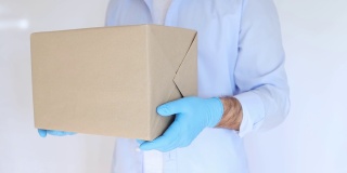 拿着纸盒，戴着医用手套的送货员。快递，网购。冠状病毒捐赠箱。交付的食物。食物的帮助。
