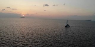 无人机在印度洋，马尔代夫，达拉万胡美丽的橙色日落期间环绕着帆船。晚上有些云和小波浪。