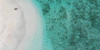无人机拍摄的情侣在美丽的沙滩上行走的视频。航拍的男人和女人手牵手在沙滩上，印度洋，马尔代夫。水位上升的孤岛旅游目的地。