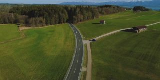 乡村街道道路穿过基姆湖的绿色农田和著名的赫伦基姆湖城堡岛无人机飞行在巴伐利亚充满活力的春天春天在德国。远处的巴伐利亚阿尔卑斯山脉。路德维希国王二世凡尔赛宫