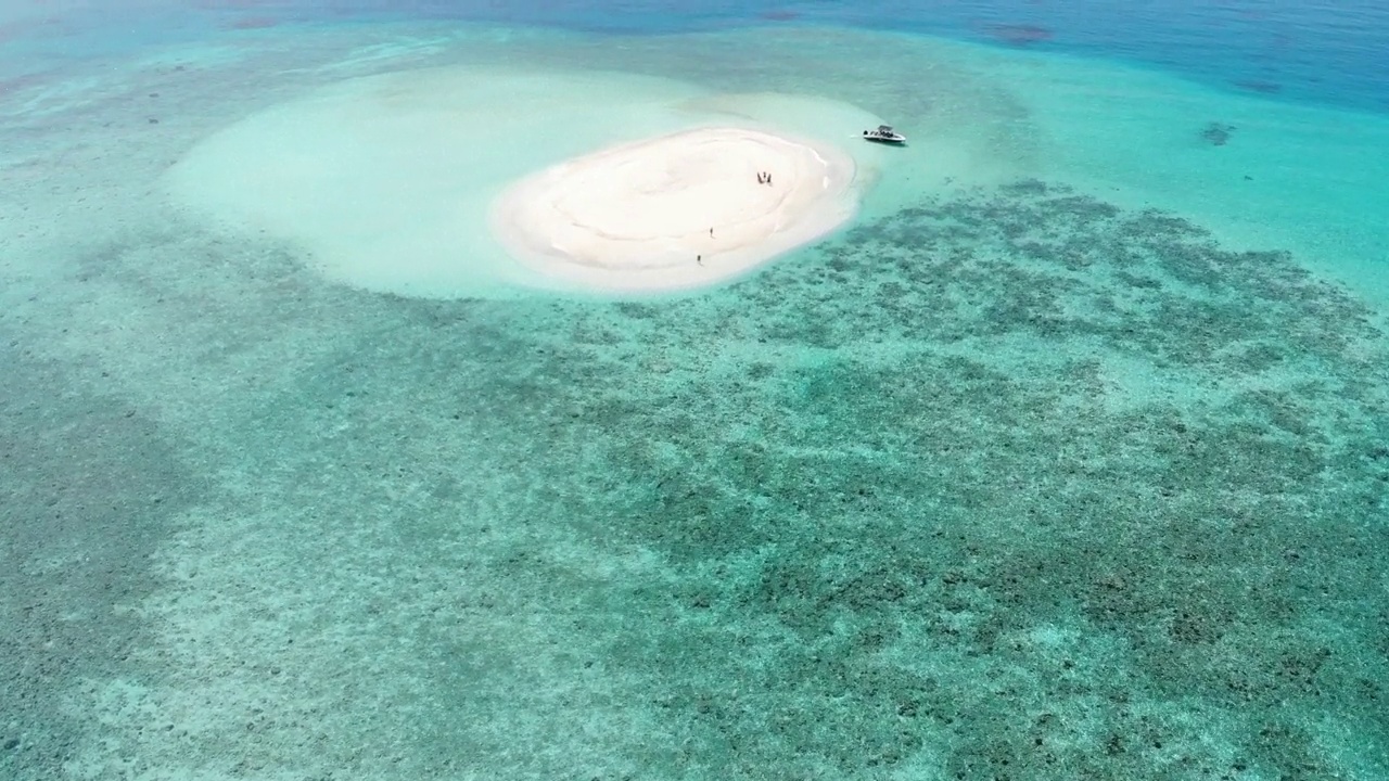 无人机飞过白色沙滩和蓝绿色海水的圆形沙洲，马尔代夫达拉万胡。只有一艘船和两个人被困。