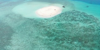 无人机飞过白色沙滩和蓝绿色海水的圆形沙洲，马尔代夫达拉万胡。只有一艘船和两个人被困。