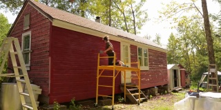 时间的推移，人们在一个农场粉刷一个小木屋红色