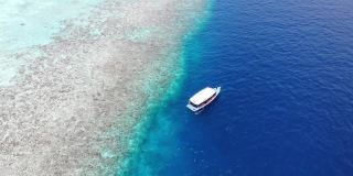 无人机在热带岛屿上空飞向漂浮在深蓝色海水上的水肺潜水船，Alif Alif环礁，Rasdhoo，马尔代夫，印度洋。白沙碧水。