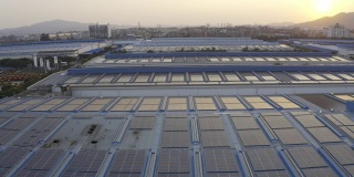 太阳落山时，太阳能电池板安装在一家大型工厂的屋顶上的航拍照片