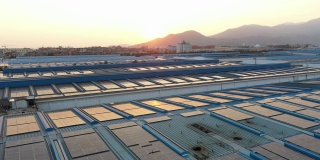 太阳落山时，太阳能电池板安装在一家大型工厂的屋顶上的航拍照片