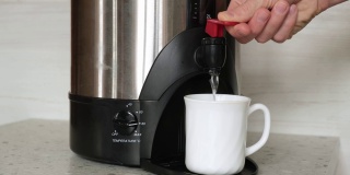 4 k。特写镜头:一个男人的手从一个热水壶里往一个白色杯子里倒茶或咖啡的热水。