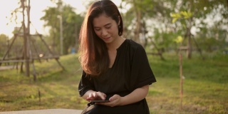 亚洲女性成熟在公园使用手机。成年女性手持手机，伴着美丽的阳光。