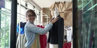 快乐的年轻亚洲女裁缝时装设计师正在检查为完成一套西装和连衣裙在一个陈列室。成功的概念年轻企业家在时尚行业。