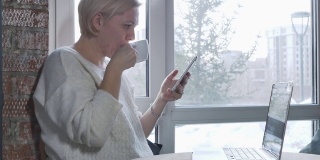 冬日里，窗前的咖啡馆里，一个年轻女子拿着笔记本电脑和智能手机