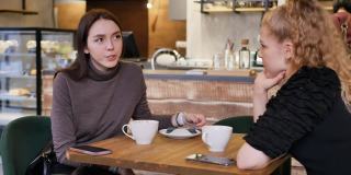 一个年轻的金发和黑发女人坐在餐厅的桌子边喝茶聊天