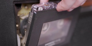 女人的手从一台老式录音机里拿出一盒老式录音带。4K