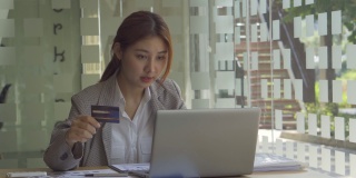 亚洲妇女持有信用卡使用移动电话在白色房间移动在线支付和簿记在办公室与笔记本电脑和图形文件在计算分析业务概念表。