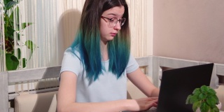疲惫的十几岁的女孩看着笔记本电脑，而坐在桌子旁。学习期间过度劳累，准备考试。倦怠而学习。心理健康的概念。