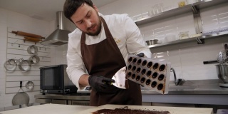 糕点师用抹刀从糖果模中取出多余的巧克力。