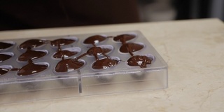 一个糕点师用融化的巧克力填充糖果模具的特写镜头。