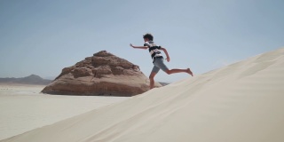 迷人的小男孩跑下沙丘与岩石沙漠慢镜头