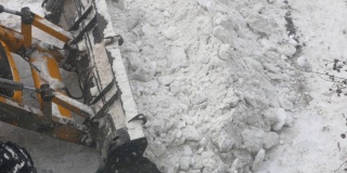 冬天用水桶除雪设备。一辆带着铲斗的拖拉机从路上铲走一堆雪。下雪后打扫街道。全景相机运动