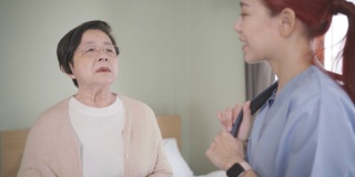 年长亚洲妇女与亚洲妇女护士在卧室穿着手术服交谈。看护者上门探访。家庭保健和养老院的概念。慢动作的4 k的视频。