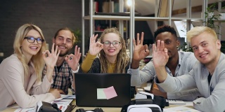 在当代办公室里，一群面带微笑、充满创意的朋友以OK的姿势在镜头前摆姿势