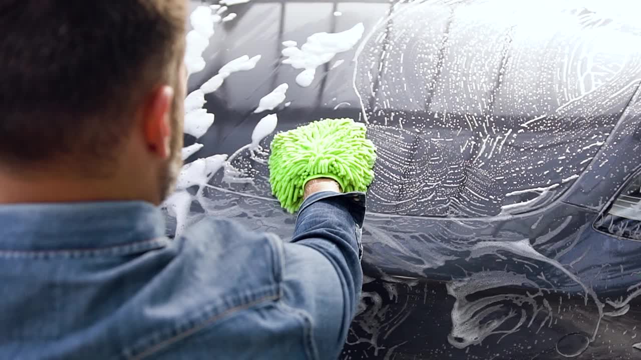 年轻英俊的大胡子男子在户外洗车时用泡沫海绵洗自己的车