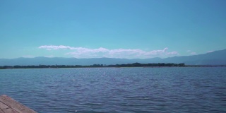 从一艘木船在一个大的湖上旅行，背景是山和多云的天空。