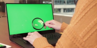 年轻女子在笔记本电脑上打字，拿着放大镜检查绿色屏幕上的东西，把它拿近一点。色度键,模型