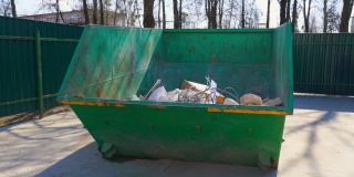 城市街道上的大型绿色金属垃圾箱，里面有建筑垃圾。