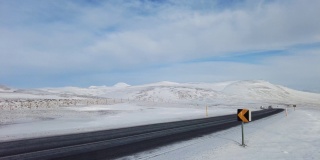 广角拍摄的汽车行驶在冰岛路上，雪山和日落乡村，冬天的时间。4 k