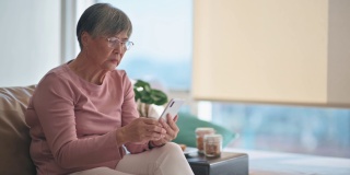 亚洲华人老年妇女使用智能手机阅读短信在她的公寓在城市