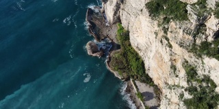 从空中俯瞰，海浪拍打着蓝色海洋中的岩石。海浪在美丽的海滩鸟瞰图无人机。从上方鸟瞰海浪撞击空岩悬崖的景象。