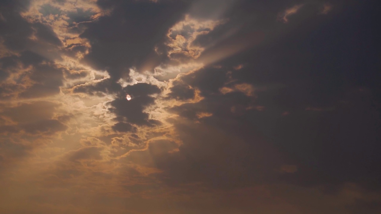 日落时，太阳在云层后面放射出太阳光的特写镜头。阳光穿过云层。自然背景