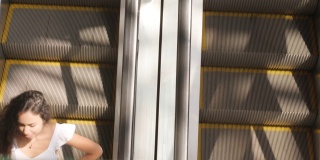 一名年轻女子提着五颜六色的购物袋在自动扶梯上逛商场