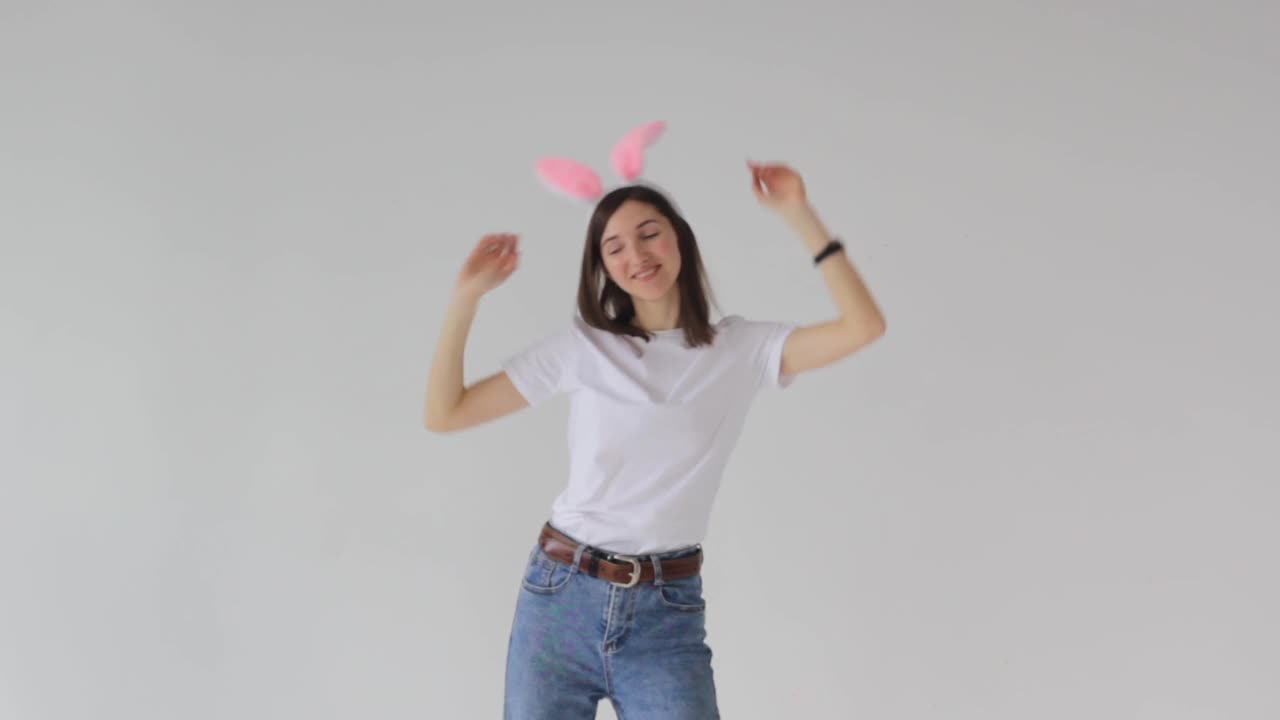 一名头上戴着兔耳的美丽女子在摄影棚的白色背景上欢快地跳舞。