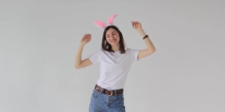 一名头上戴着兔耳的美丽女子在摄影棚的白色背景上欢快地跳舞。