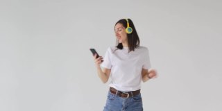 一个穿着白色t恤的漂亮年轻女子戴着耳机听音乐，看着手机，跳舞，闲逛。