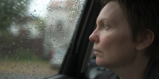 悲伤的女商人等在车里，在雨中看着窗外