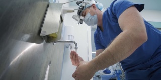 外科医生在现代化的手术室里为手术做准备，清洗和消毒双手。医生配备口罩、医用头灯、手术放大镜