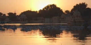 在印度拉贾斯坦邦Jaisalmer的加迪萨尔湖，日落时分，恰特里站在湖中央。日落时，恰特里亭在橘黄色湖水中的倒影。