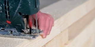 一个女人的手用电动拼图切割一块板的特写。木工用工具在木头上，锯屑飞扬，锯切成直线。家里用自己的手修理，一个锯木厂。慢动作