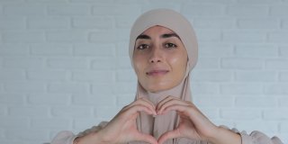 可爱的穆斯林阿拉伯妇女，戴着头巾，用手表达爱意，浪漫的情感，可爱的，幸福的，和平的姿态。全世界的爱，是穆斯林妇女对全世界的爱的象征
