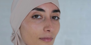 年轻漂亮的穆斯林女子自信地微笑着，戴着伊斯兰教的头巾，脸上露出快乐可爱的表情。根据伊斯兰教法，女性的生活受到权利和自由的限制