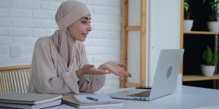 一位亲切微笑的穆斯林妇女正在手提电脑上上网，与同事进行电话会议。一位戴着头巾的美丽阿拉伯女子在一个没有偏见的新世界里使用互联网