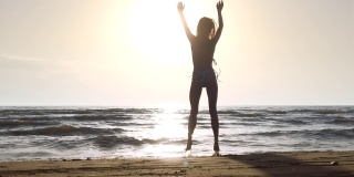 剪影女孩在海滩上的比基尼在日落，有乐趣，跳和跳舞。以120帧每秒拍摄的慢动作