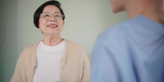 高级亚洲妇女与亚洲妇女护士在卧室穿着手术服交谈。看护者上门探访。家庭保健和养老院的概念。慢动作的4 k的视频。