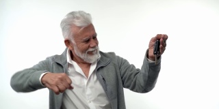 一位留着灰胡子的时尚而情绪化的老人展示了他新买的汽车钥匙。在一个白色孤立的背景。养老金领取者的趋势特征。