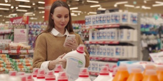 一名女子在超市购物时，用智能手机扫描一瓶洗涤剂上的条形码，查看产品信息和价格