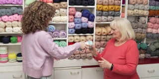 有爱心的年轻女售货员帮助女高级顾客选择羊毛的颜色